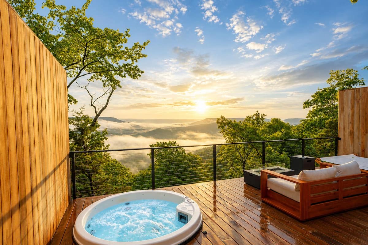 Una terraza de madera con un jacuzzi, un sofá de madera y vistas a un paisaje montañoso.