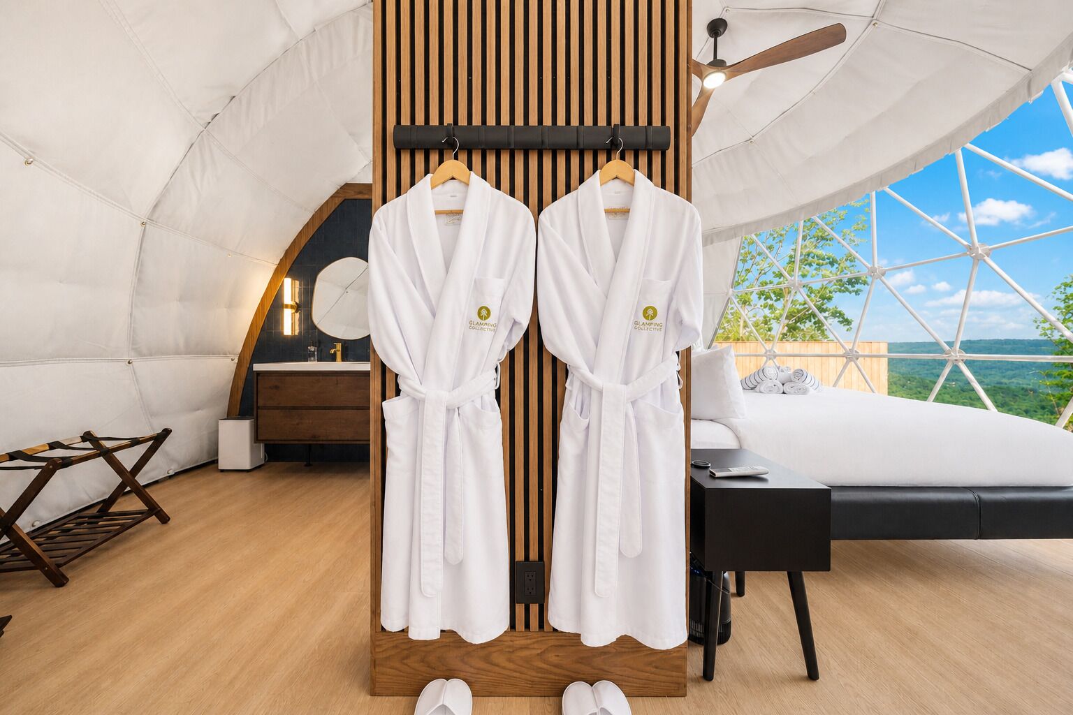 Une pièce aménagée comme une tente, avec un lit, une commode en bois et deux robes blanches suspendues à un portant.