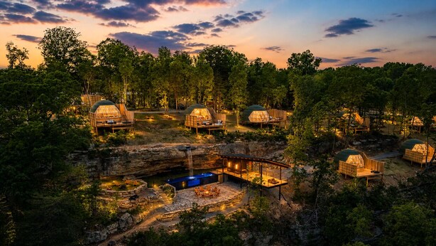 A resort with multiple dome-shaped cabins surrounded by trees, a central building with a pool, and a waterfall. - Glamping Collective Chattanooga (Trenton)