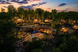 A resort with multiple dome-shaped cabins surrounded by trees, a central building with a pool, and a waterfall. - Glamping Collective Chattanooga (Trenton)