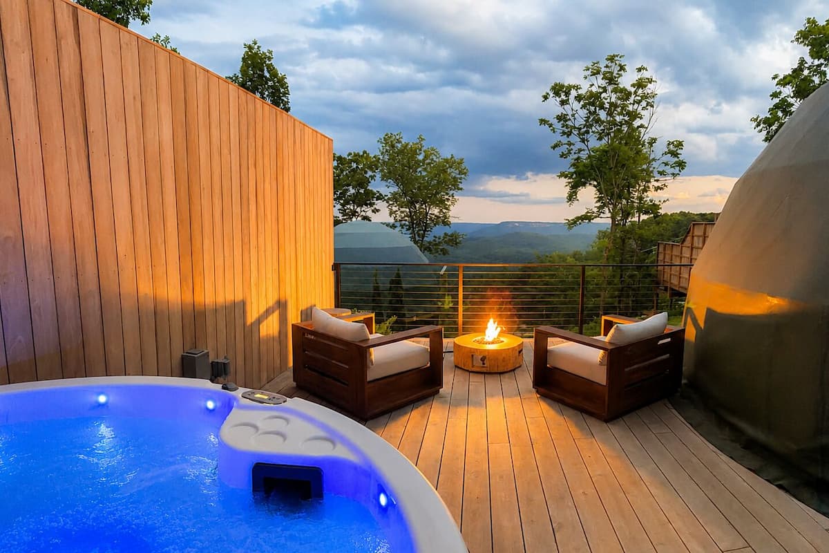 Un jacuzzi con una terraza de madera, dos sillones de descanso y una chimenea.