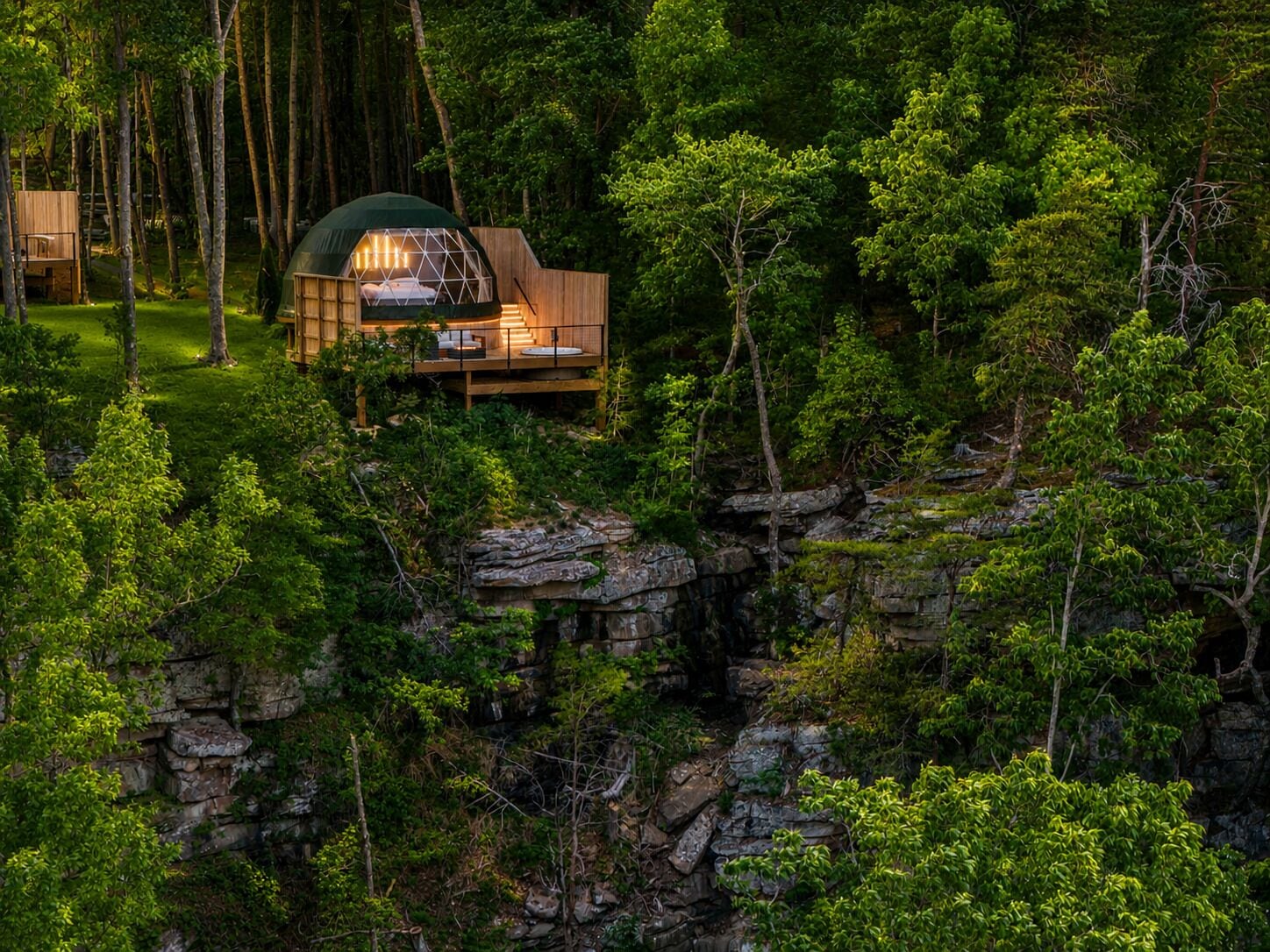 A cabin with a wooden deck, surrounded by dense forest and rocky terrain.