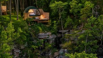 A cabin with a wooden deck, surrounded by dense forest and rocky terrain.