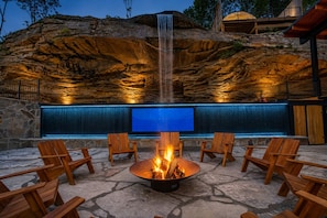 A stone fire pit with chairs around it, a waterfall, and a blue-lit wall.