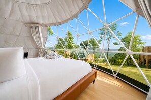 Ein Schlafzimmer mit einem großen Bett, Blick ins Freie und einer geometrischen Fenstergestaltung.