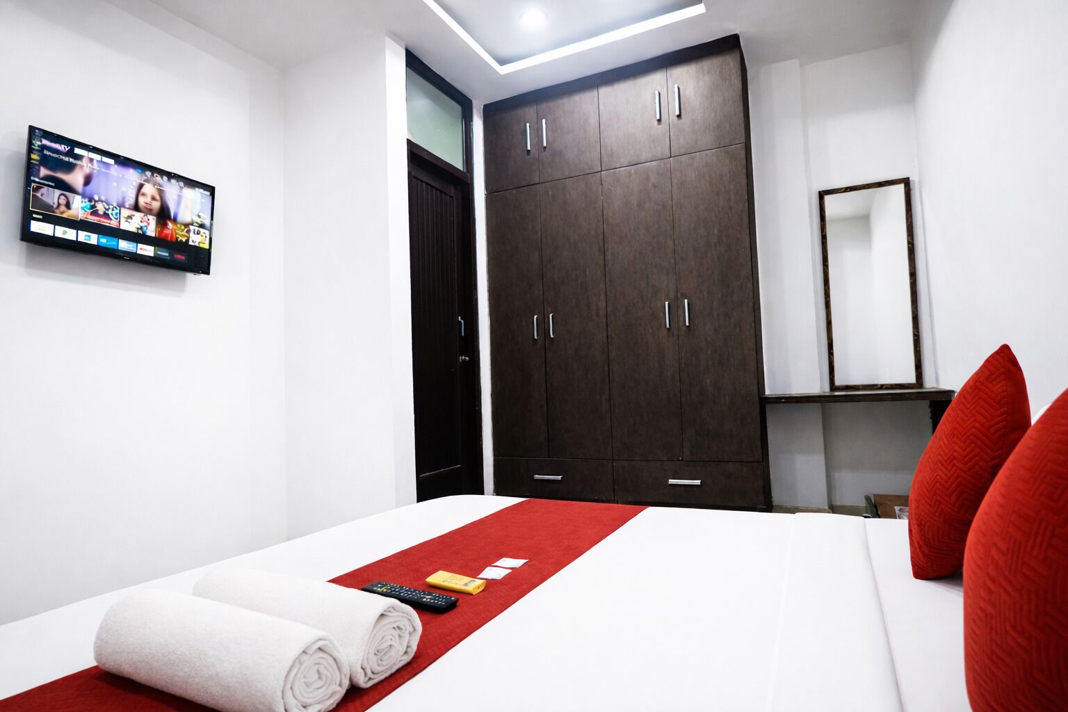A hotel room with a bed, a TV mounted on the wall, a wardrobe, and a mirror.