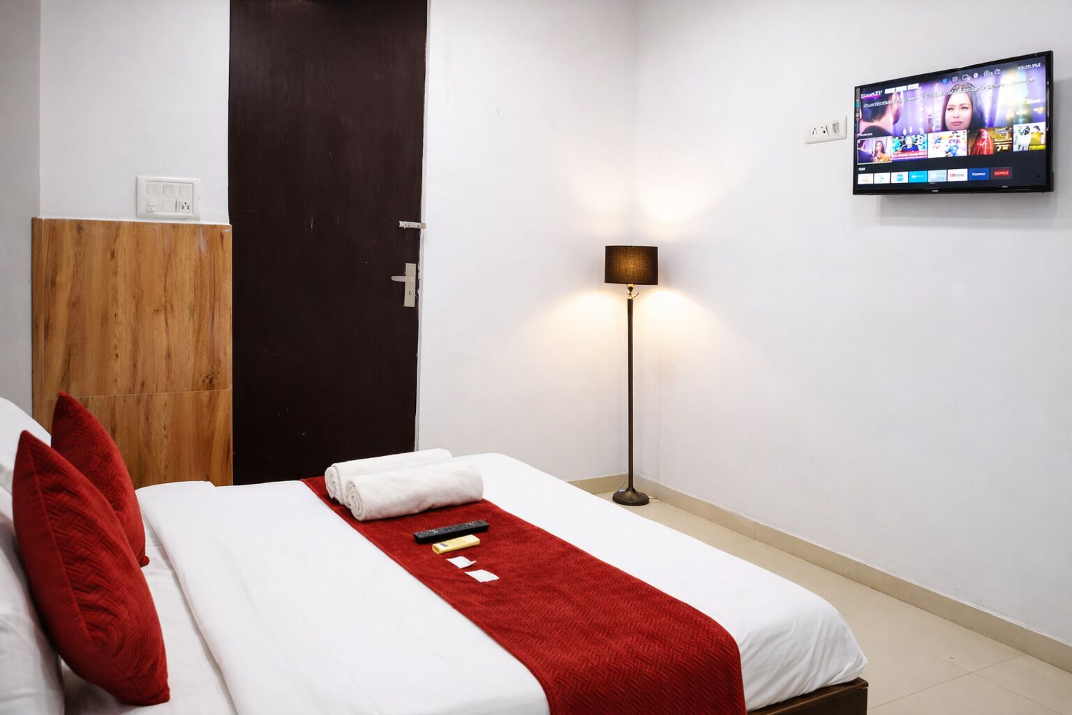 A hotel room with a bed, a TV, a lamp, and a wooden wardrobe.