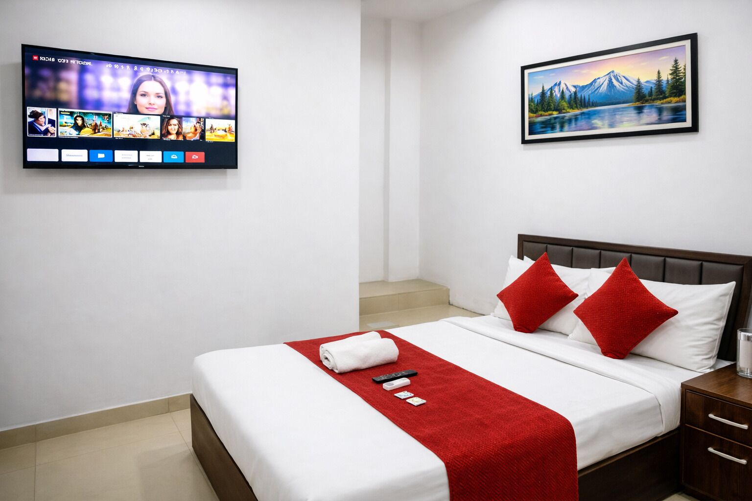 Habitación de hotel con una cama, un televisor montado en la pared y un cuadro sobre la cama.