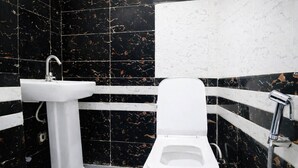 Une salle de bain avec un lavabo sur colonne blanc, des toilettes et des murs recouverts de carreaux noirs et blancs.