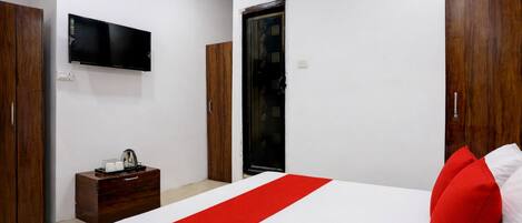 A hotel room with a bed, a TV, a wooden wardrobe, and a small table with a coffee maker.