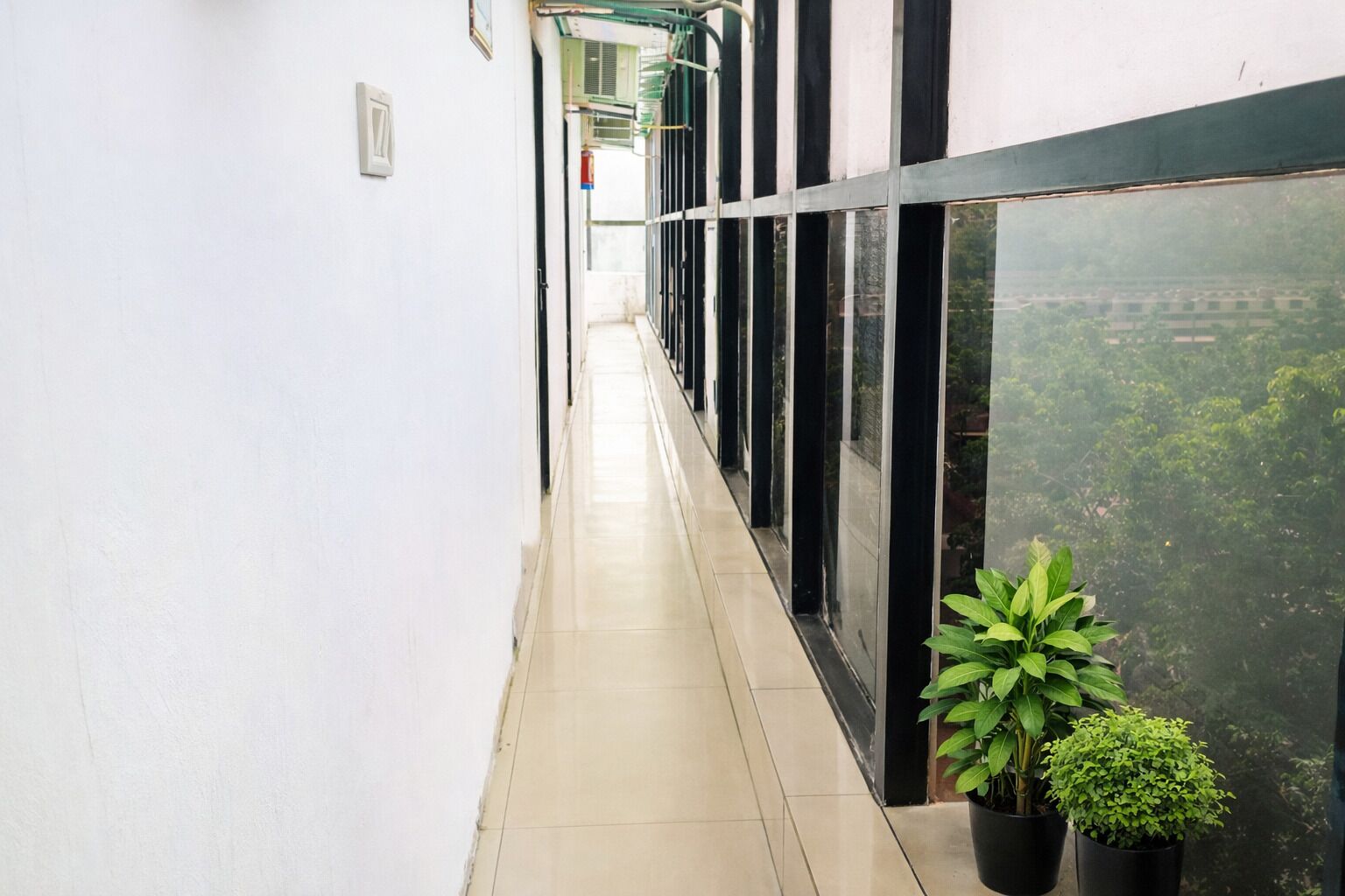 A corridor with a tiled floor, large windows, and potted plants.