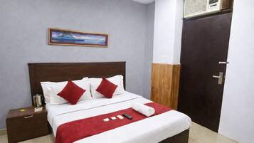 A neatly made bed with white and red bedding, a wooden headboard, a nightstand with a metal pitcher, and a painting on the wall.