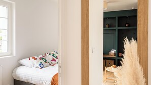 Un dormitorio con cama, ventana y puerta que da a una habitación con estanterías y una mesa.