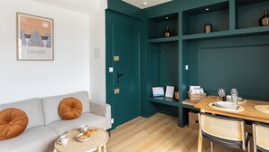 Un interior moderno con una pared de acento color turquesa, un sofá con cojines naranja, una mesa de comedor lista para dos personas y un cuadro en la pared.