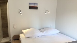 Ein Hotelzimmer mit Bett, einer Bank, einem Bild an der Wand und einer Duschkabine.