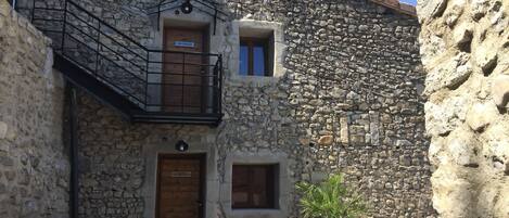 Un bâtiment en pierre avec une porte en bois, un petit balcon et une plante en pot rouge.