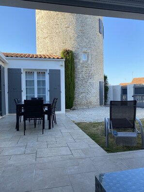 Une terrasse avec une table et des chaises en pierre, un mur en pierre et une petite fenêtre.
