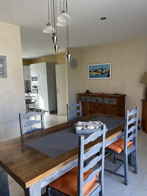 Un coin repas avec une table en bois, des chaises rembourrées de couleur grise, un plateau rempli de coquillages, une horloge et un tableau accroché au mur.
