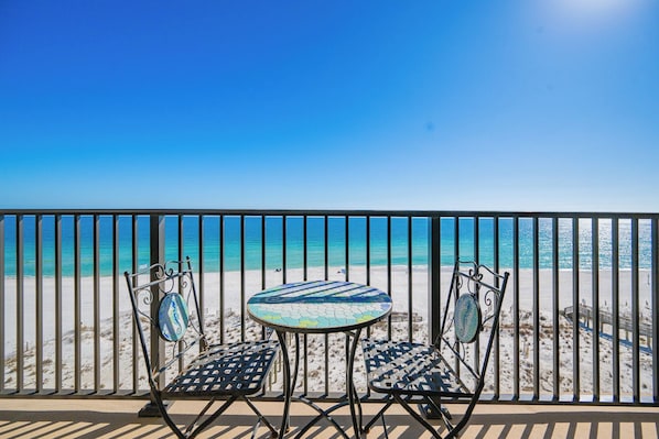 Ein Balkon mit Blick auf den Strand, zwei Stühle und ein kleiner Tisch.