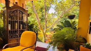Une chaise jaune dans une pièce donnant sur un jardin, un meuble décoratif et une plante en pot posée sur une table.