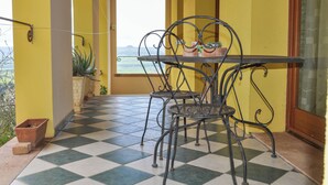 A balcony with a checkered floor, a metal table with chairs, a potted plant, and a view of the sea. - Il Glicine (Laconi)