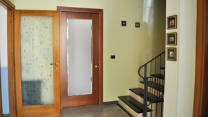 A hallway with a wooden door, a staircase, and a wall with framed pictures. - Il Glicine (Laconi)
