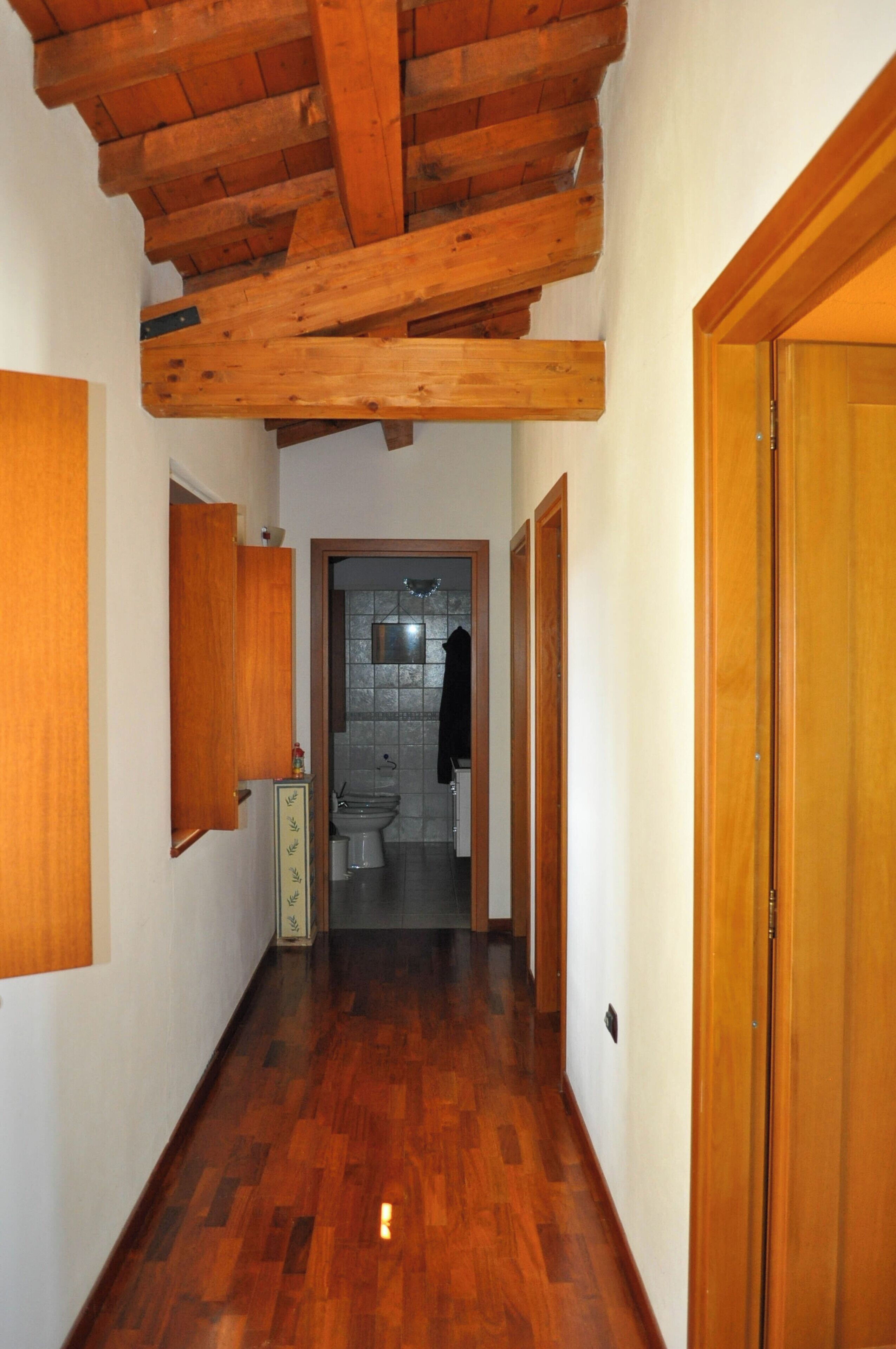 Un pasillo con suelo y techo de madera, y una puerta que da al baño.