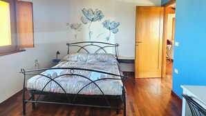A bedroom with a wooden ceiling, a metal bed frame, a blue floral wall decoration, and a wooden door. - Il Glicine (Laconi)
