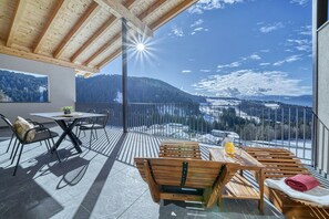 Un balcón con vistas a un paisaje nevado de montañas, una mesa con sillas y un banco.
