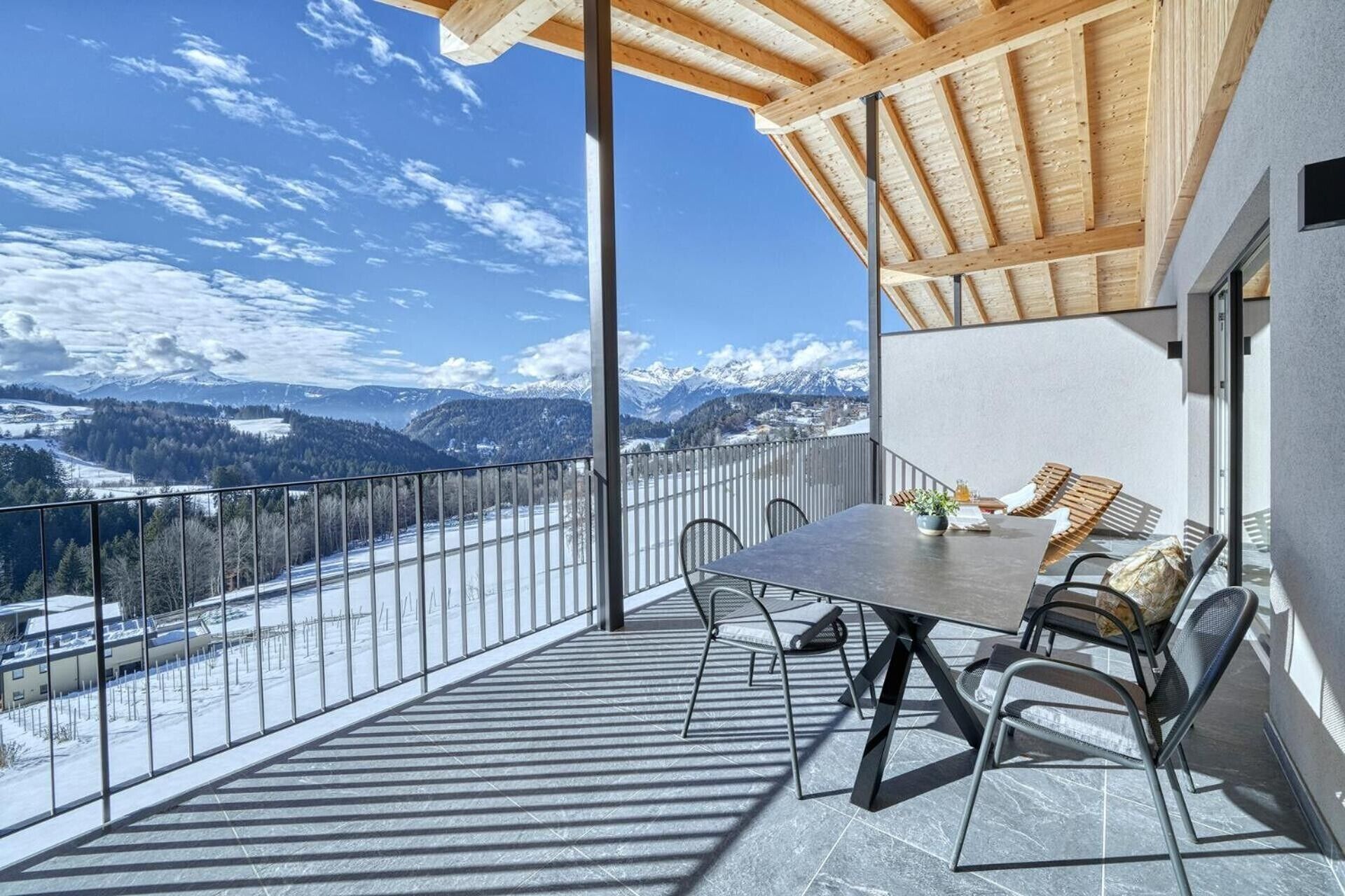 A balcony with a table and chairs, a view of snow-covered mountains, and a clear sky.