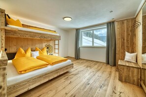 Una cama litera con ropa de cama amarilla, un cabecero de madera, una ventana con vistas a un paisaje nevado y una pared de madera con un estante.