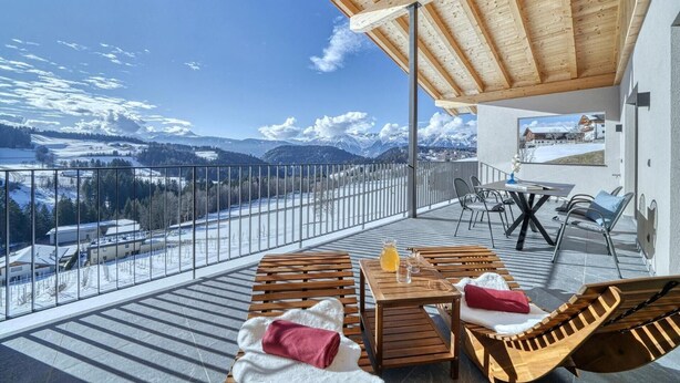 A balcony with a wooden table, chairs, and a view of snow-covered mountains. - Bright Apartment with 2 Bedrooms & Mountain Views – Montes (Avelengo)