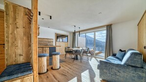 A modern interior with a wooden accent wall, a dining area with a view, and a sofa. - Bright Apartment with 2 Bedrooms & Mountain Views – Montes (Avelengo)