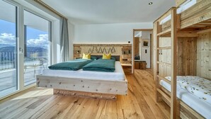A bedroom with a wooden bed, a balcony with a view of mountains, and a wooden headboard. - Beautiful Apartment with Mountain View – Silva (Avelengo)