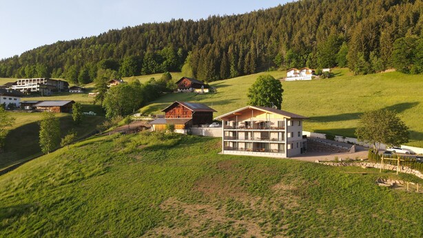 A multi-story building with a balcony, surrounded by green fields and a forested hill. - Beautiful Apartment with Mountain View – Silva (Avelengo)