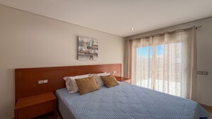 Een slaapkamer met een bed, een nachtkastje, een kunstwerk aan de muur en een raam met gordijnen.