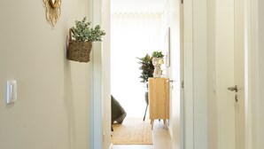 Un pasillo con un tapiz tejido, una cesta de mimbre con plantas y un mueble de madera con una planta.