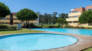 Una piscina con muelle de madera, rodeada de vegetación y edificios modernos.