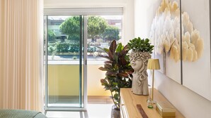 Una habitación con un ventanal grande, una planta en maceta, una estatua y una lámpara sobre una mesa de madera.
