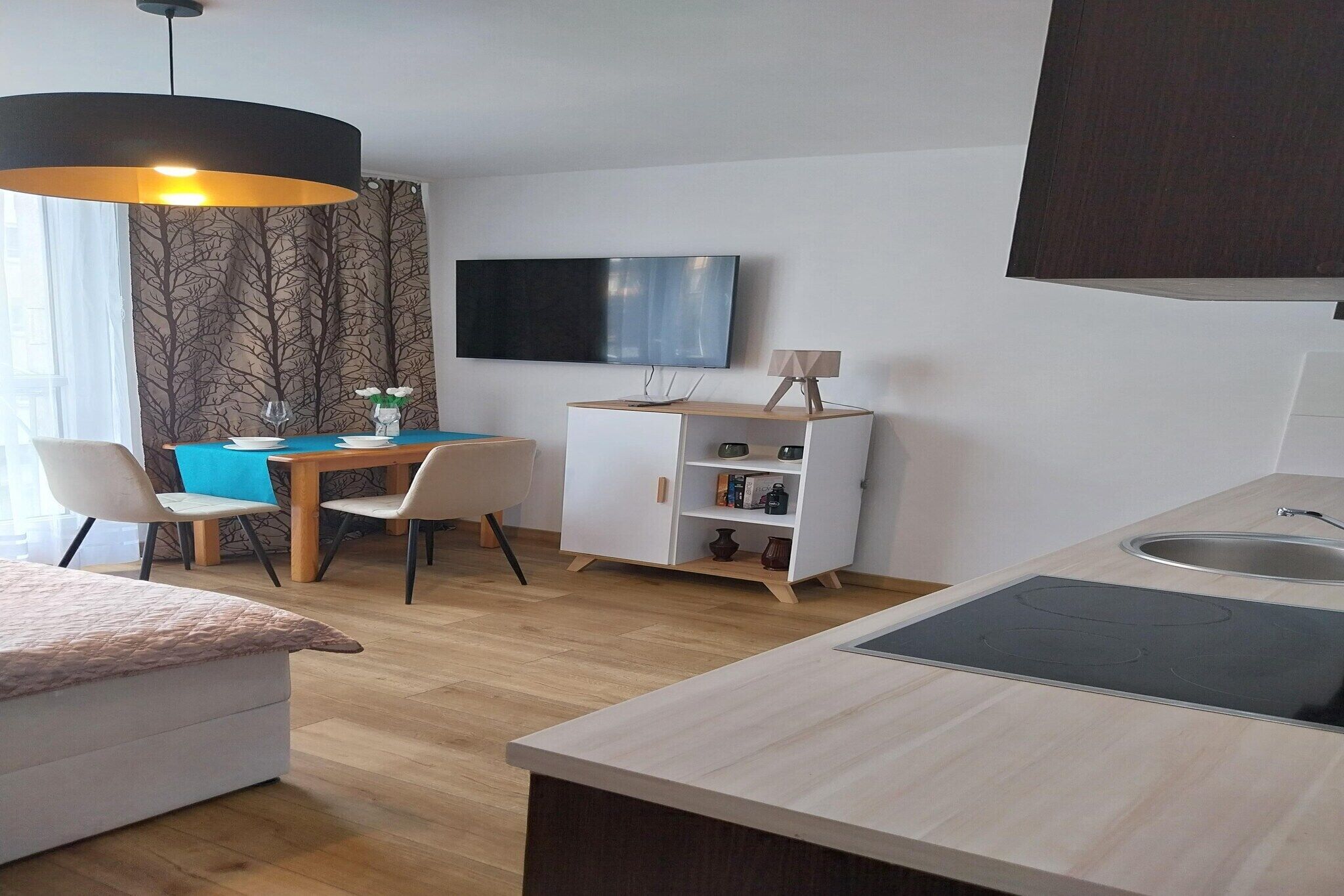 A modern kitchen with a built-in stove, a dining area with a table and chairs, and a TV mounted on the wall.