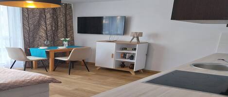 A modern kitchen with a built-in stove, a dining area with a table and chairs, and a TV mounted on the wall.
