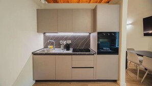 A compact kitchen with a built-in oven, a countertop with a sink, and a dining area with a table and chairs.