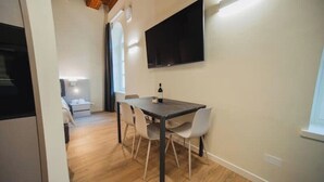 A modern kitchen with a dark countertop, a dining area with a table and chairs, and a flat-screen TV mounted on the wall.