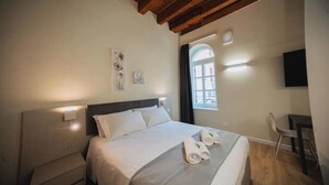 A hotel room with a bed, bedside table, and a desk with a chair.