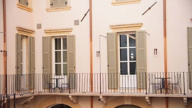 A building with multiple windows, a balcony with chairs, and an arched entrance.