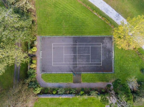 An aerial view of a tennis court surrounded by green grass and trees.