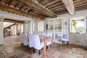 Un coin repas avec une table en bois dressée pour six personnes, des chaises blanches et une vue sur une forêt par la fenêtre.