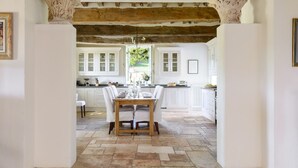 Une cuisine avec des meubles blancs, un sol en pierre et une table en bois mise pour le repas.