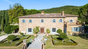 Un bâtiment en pierre doté d’une façade symétrique, de nombreuses fenêtres avec volets, d’une entrée centrale et d’un jardin à la française avec des haies aux formes géométriques.