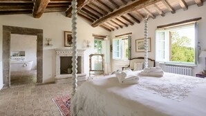 Une chambre à coucher avec un grand lit, une cheminée, une fenêtre et une porte donnant sur une autre pièce.